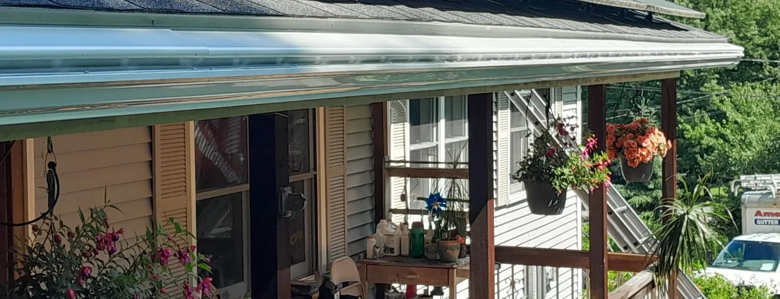 Gleaming Gutter Cap installed along a porch roofline with hanging flower baskets below