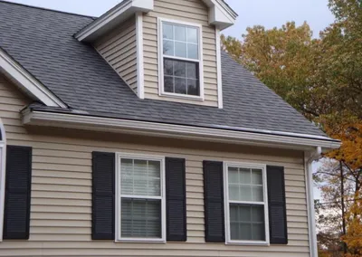 Gutter Cap installed on a tan house with black shutters