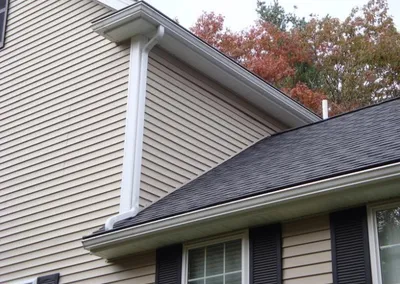 Gutter Cap and white downspout at the corner of a tan house