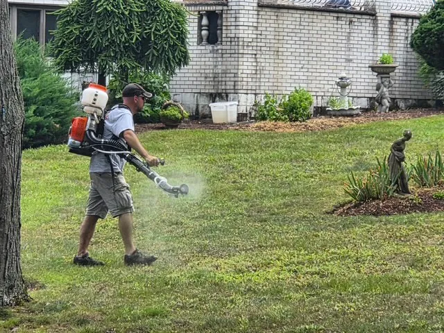 Licensed technician with a backpack sprayer treating a backyard lawn for mosquitoes and ticks