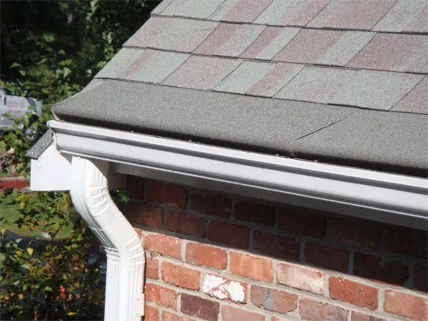 Gutter Roof cover installed on a gutter and downspout against a brick wall