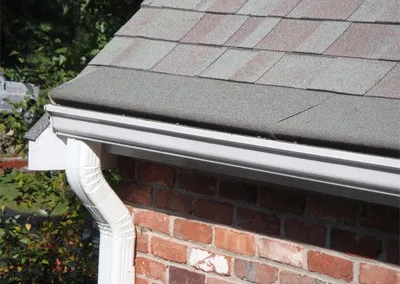 White Gutter Roof and downspout against a brick chimney