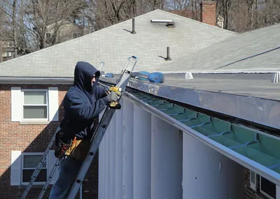Installer on a ladder fastening a new seamless gutter at the roof edge