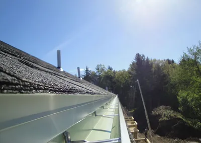 Roof-edge view of a freshly hung seamless gutter