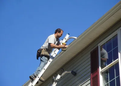 Installer working from a ladder at a second-story roofline