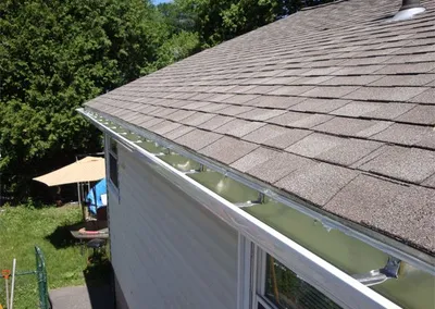 New white seamless gutter along the hip roof of a yellow house