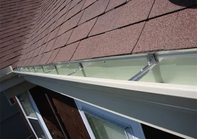 Corner detail of a new white gutter against dark red shingles